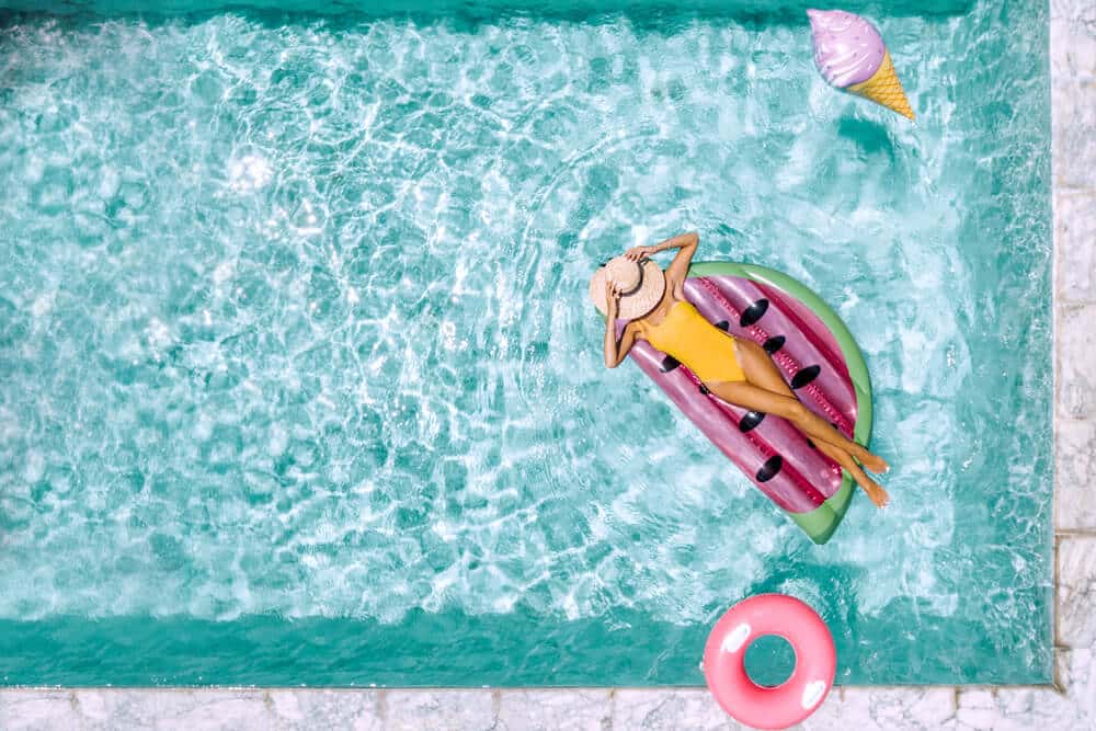 Woman relaxing on watermelon lilo in the pool at private villa. Inflatable ring and mattress. Summer holiday idyllic. High view from above.