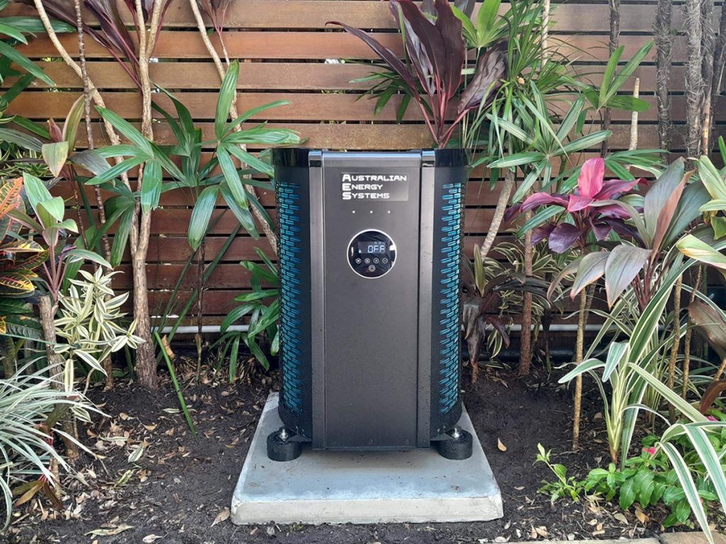 Black AES pool heat pump installed on a concrete pad in a garden